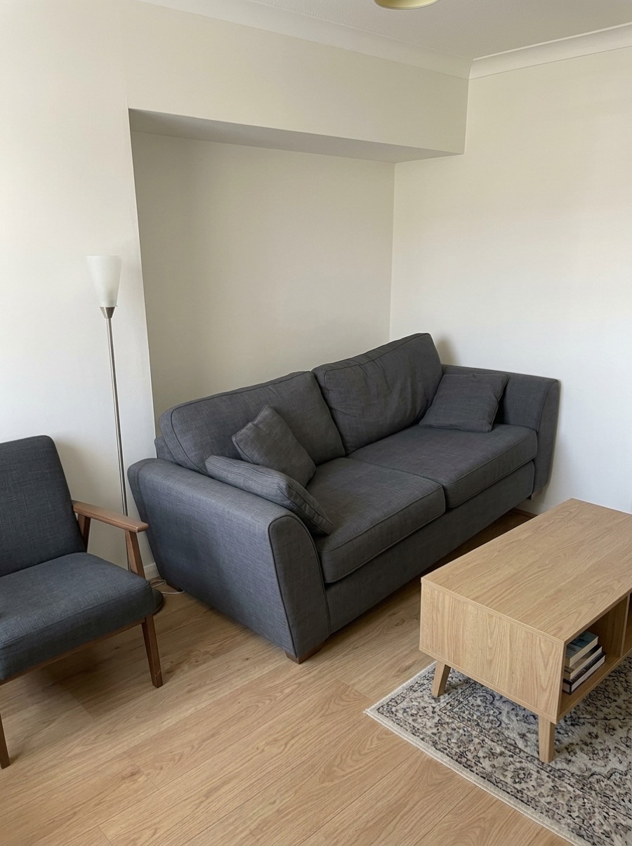 A dark grey three-seat sofa standing at an angle in a shallow wall alcove, its left arm sticking out past the edge of the recess.